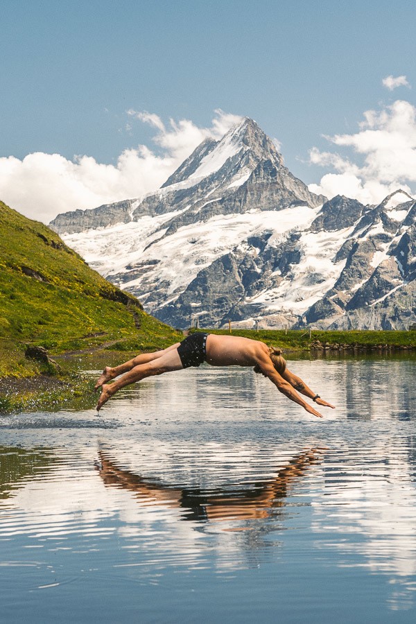 a man diving into a lake with a mountain in the background.
