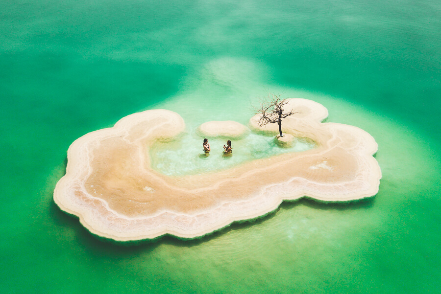 a couple of people standing on top of a sandy island.