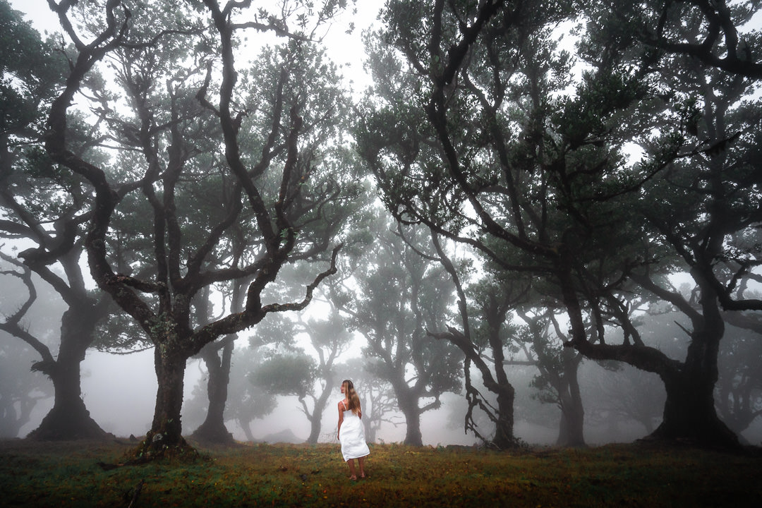 a woman in a white dress walking through a forest.