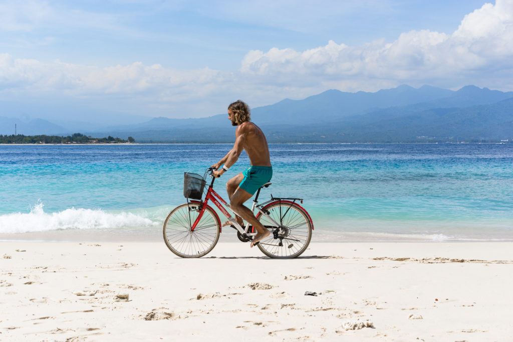 a man riding a bike on a beach next to the ocean.