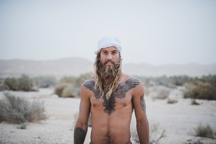 a man with long hair and a beard standing in the desert.