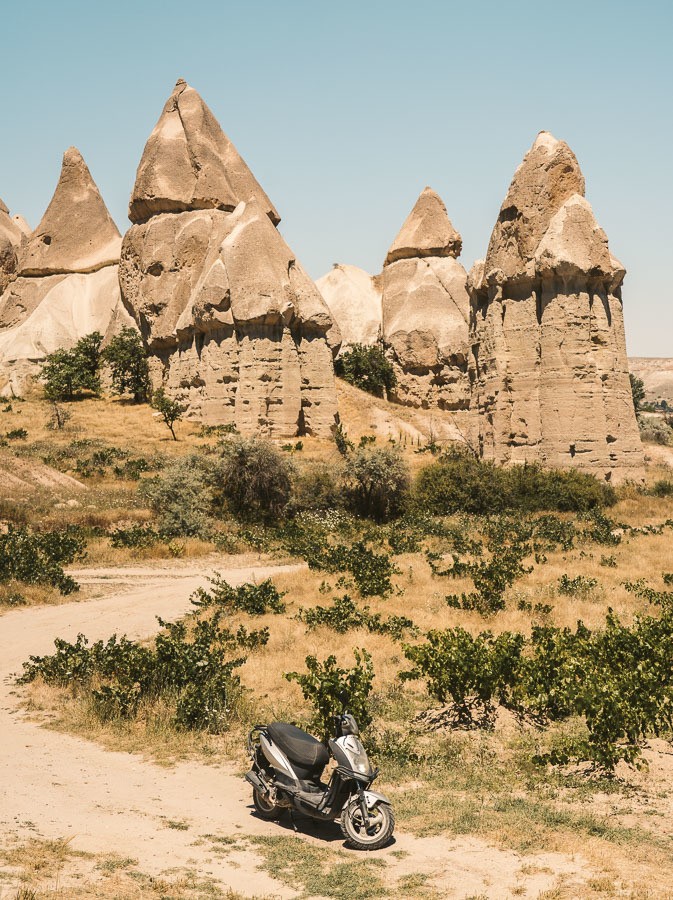 a motorcycle parked on a dirt road in front of rock formations.
