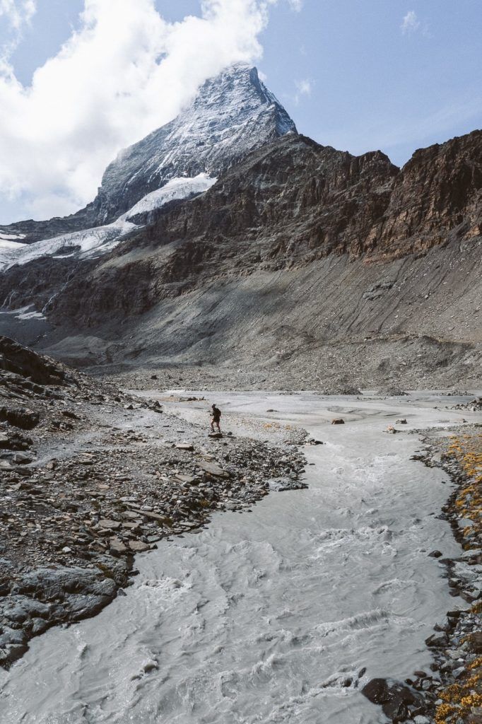 a person walking across a river in front of a mountain.