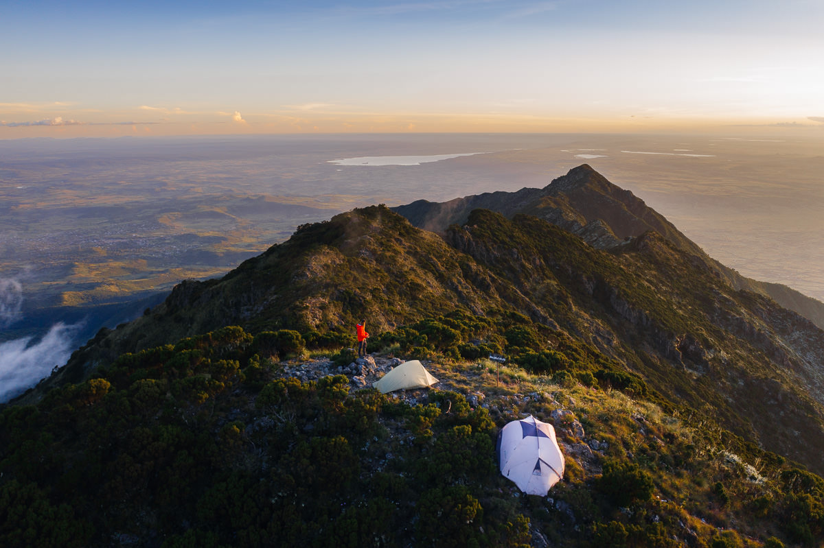 a man sitting on top of a mountain next to a tent
