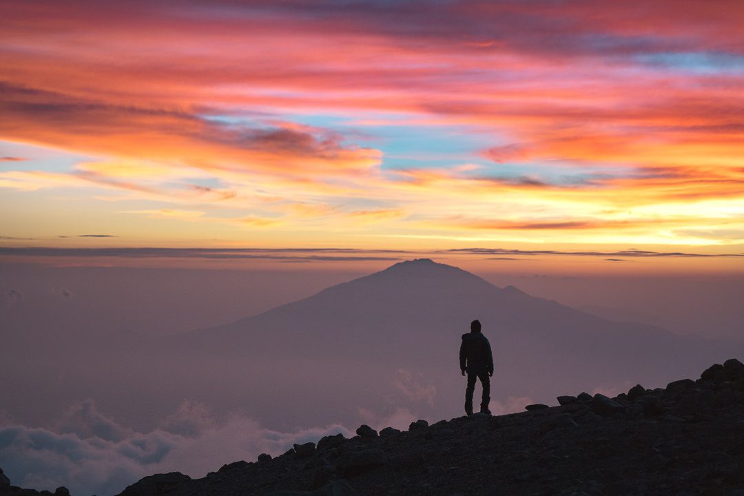 a person standing on top of a mountain at sunset.