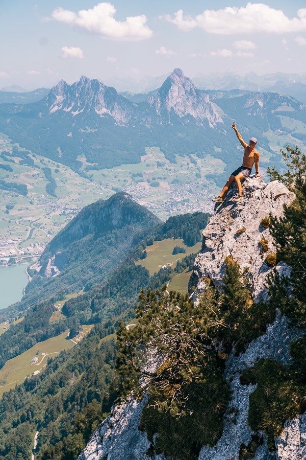 a man sitting on top of a mountain with his arms in the air.