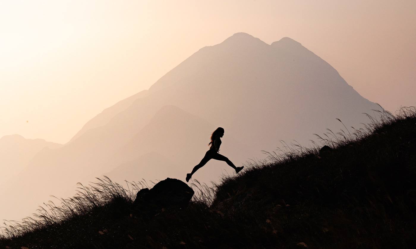 a person running up a hill with a mountain in the background.