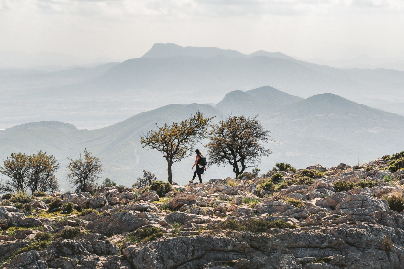 a person walking on a rocky hill with a view of mountains.